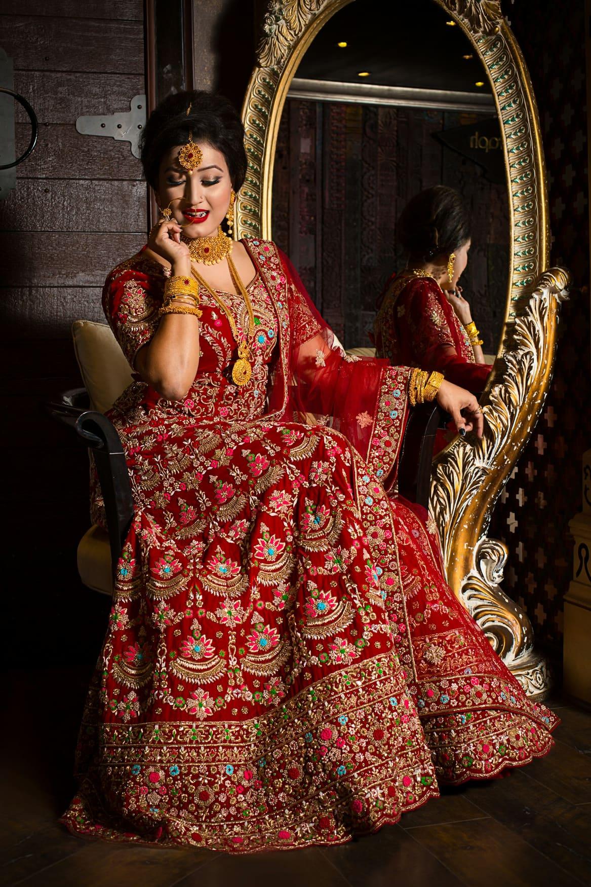 Bride in a deep maroon velvet lehenga seated on an ornate gold chair