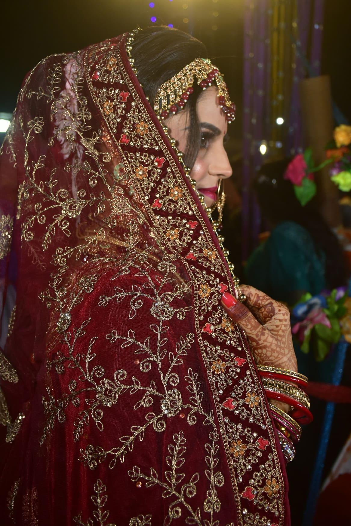Bride in a deep maroon velvet lehenga seated on an ornate gold chair — view 2 of 2