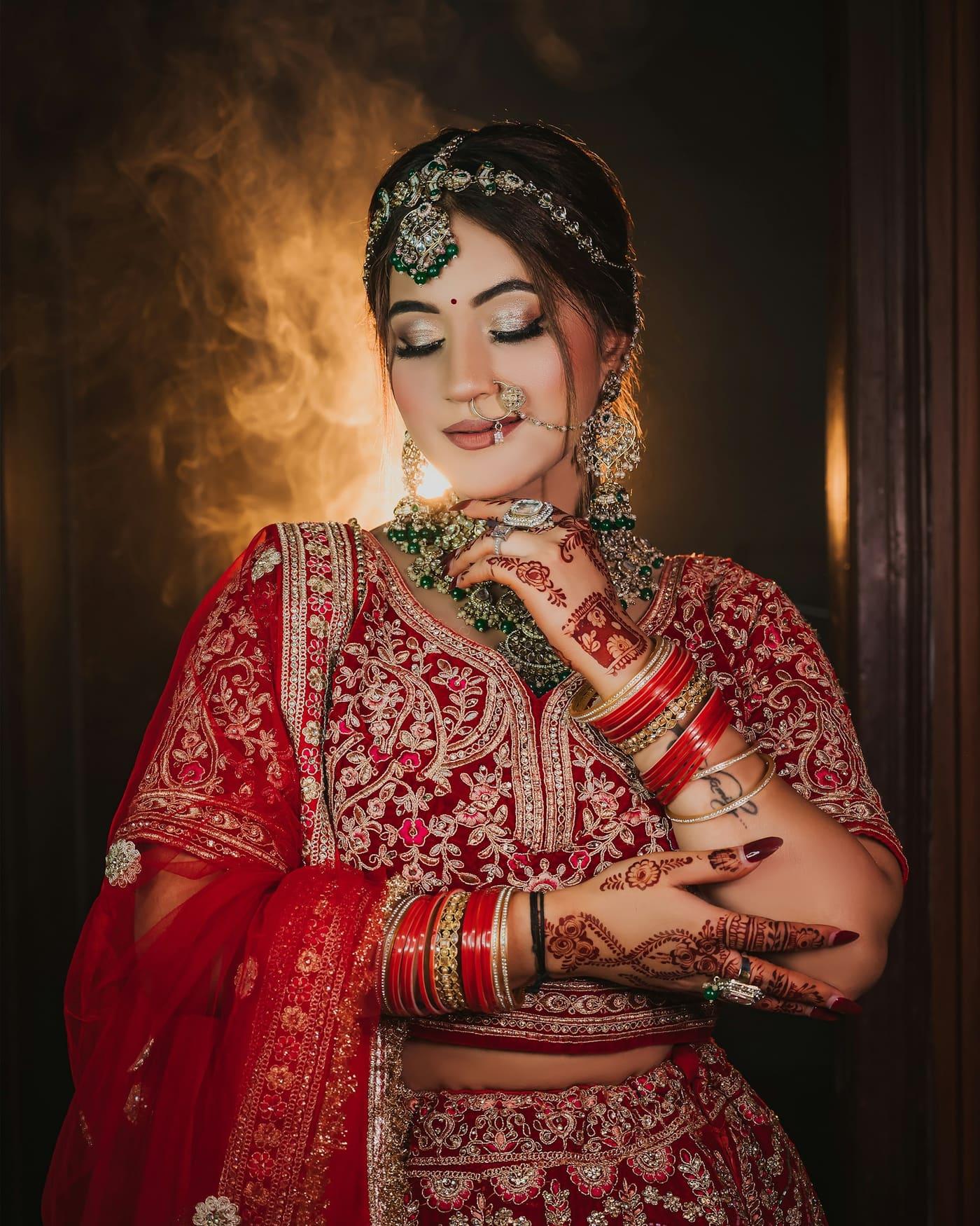 Bride in a red lehenga with gold embroidery and emerald kundan jewellery — view 2 of 3
